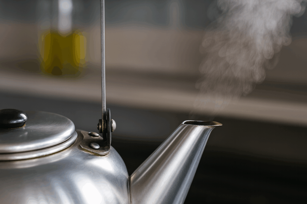 やかんの注ぎ口から湯気が立ち上る様子を横から写した写真。金属の光沢が温かみのある光で反射しており、背景はぼかされている。