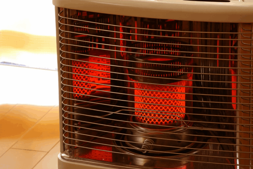 室内で赤く燃えている灯油ストーブのクローズアップ写真。金属のガード越しに炎が見え、床に暖かい光が反射している。