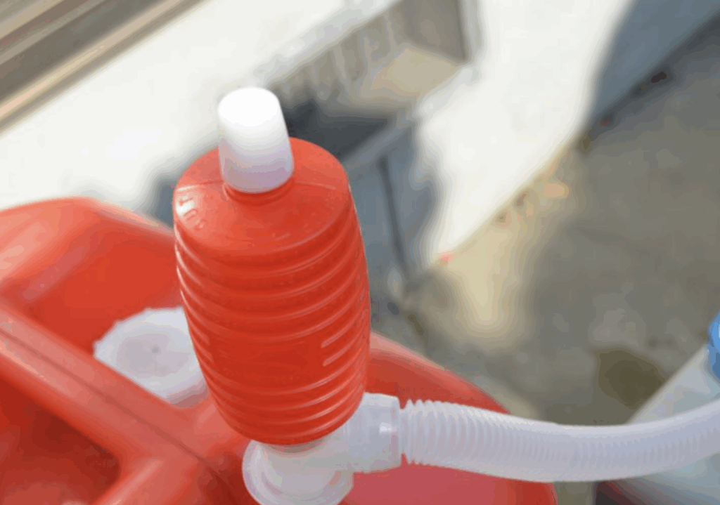 灯油ポンプを取り付けた赤いポリタンクの上部。屋外で灯油を注ぐ準備をしている様子