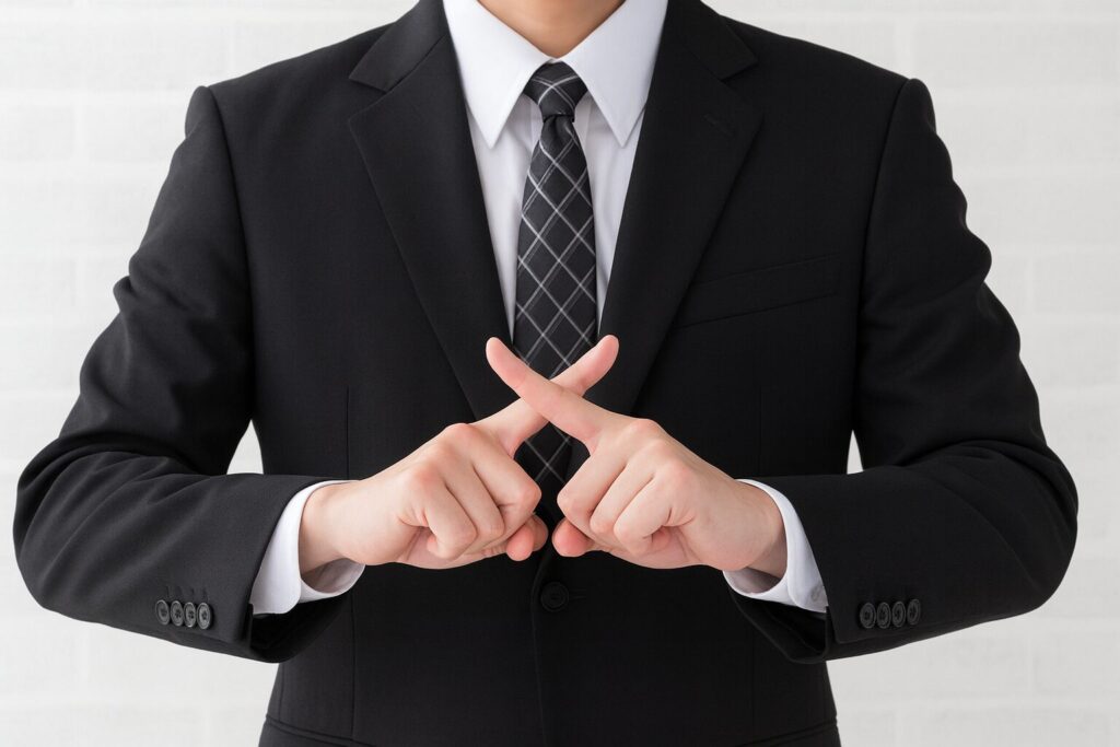 スーツ姿の男性が胸の前で指を交差させ、拒否や否定を示すジェスチャーをしている様子を写した写真