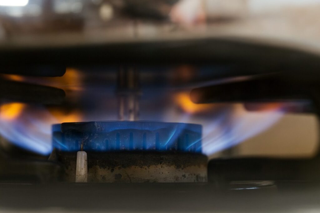 ガスコンロのバーナーから青い炎が均一に立ち上がり、点火プラグや五徳が見える近距離の様子を捉えた画像。
