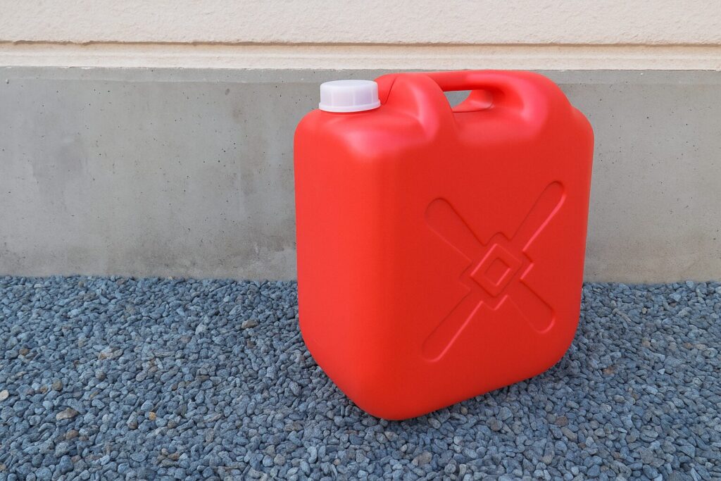 住宅の外壁前に置かれた赤いポリタンク。白いキャップ付きで、地面には青灰色の砂利が敷かれている。