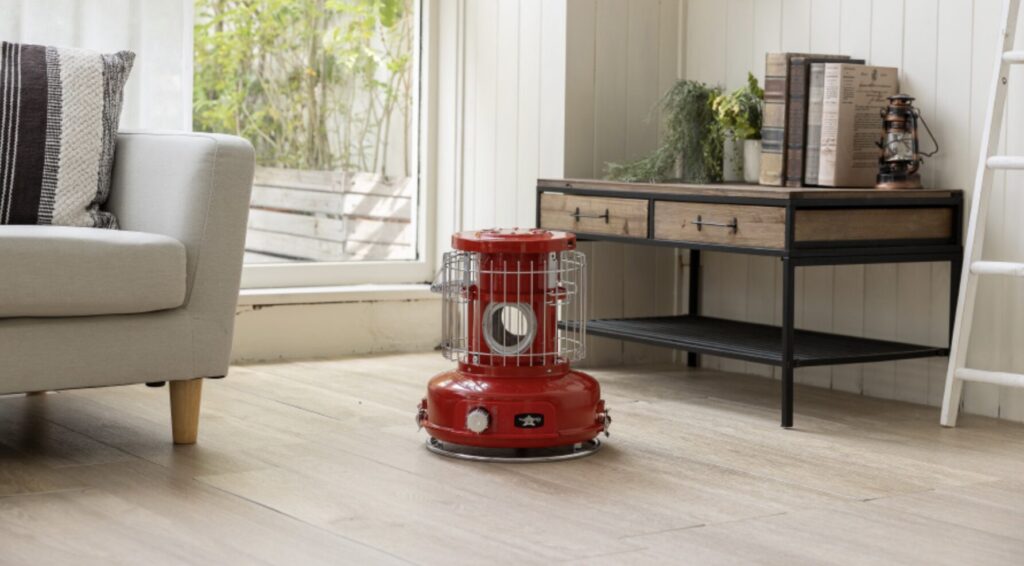 木目調の床に赤いポータブルストーブが置かれたリビングの一角。ソファや木製のサイドテーブルが並び、ナチュラルで温かみのある室内空間が広がっている。