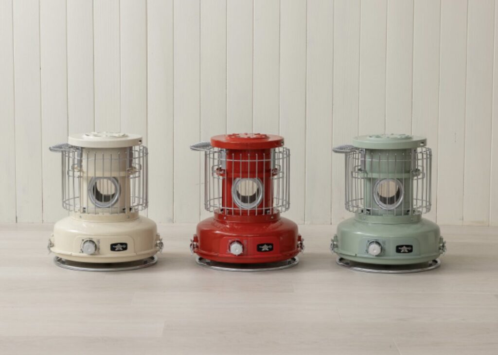 ベージュ・レッド・グリーンの3色のポータブルストーブが並べられた室内。ナチュラルな木目の床と白い壁を背景に、デザインやカラーの違いが際立っている。
