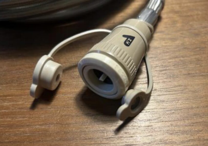 ガスファンヒーター用の迅速継手の接続口部分が、木製テーブルの上に置かれている様子。保護キャップが左右に付いており、先端の差し込み構造が見える。