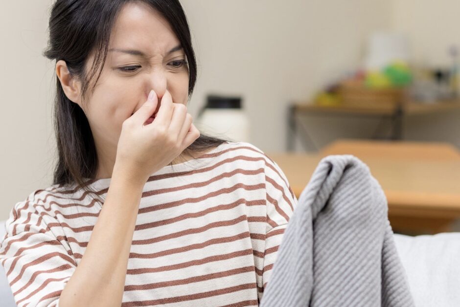 衣類のにおいに顔をしかめ、鼻をつまみながら服を見つめる女性の様子。