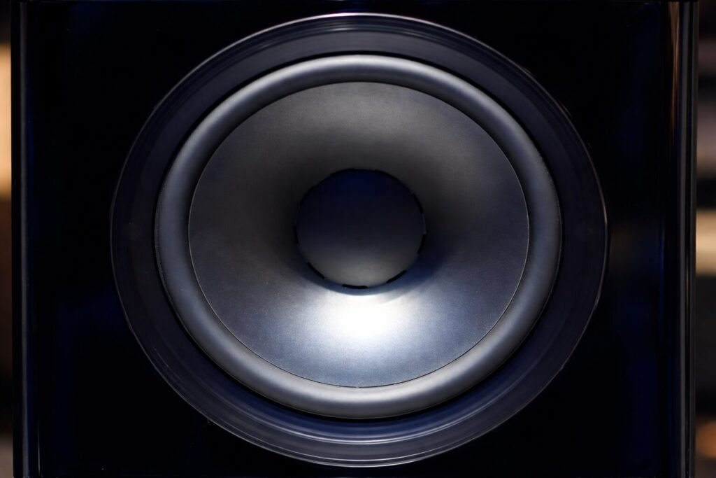 スピーカーキャビネットに組み込まれた大型ウーファーユニットを正面から捉えたクローズアップ画像で、金属調の振動板と黒いエンクロージャーの質感がはっきりと伝わる構図