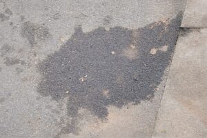 風化したアスファルトの地面に、灯油や油分が染み込んだような濃い色のシミが広がっている様子