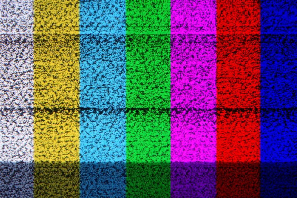 テレビのカラーバー表示が横一列に並び、白・黄・水色・緑・紫・赤・青の縦帯に砂嵐状のノイズが重なって映っている様子