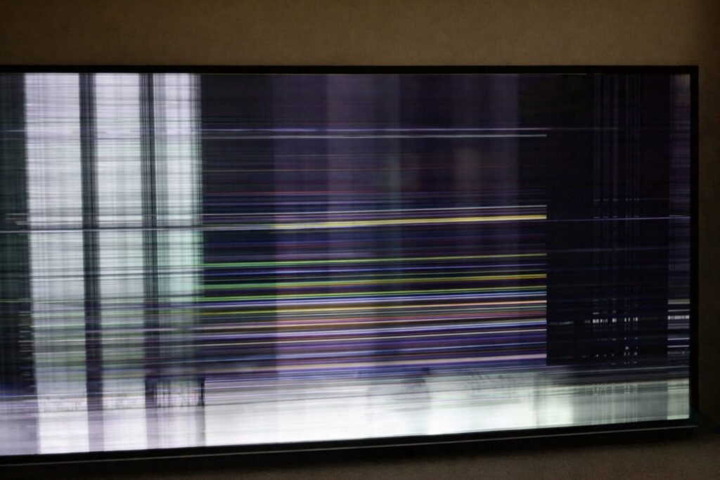 画面全体に白や紫、緑などの横線・縦線が走り、映像が大きく乱れて表示されているテレビの故障状態を写した様子