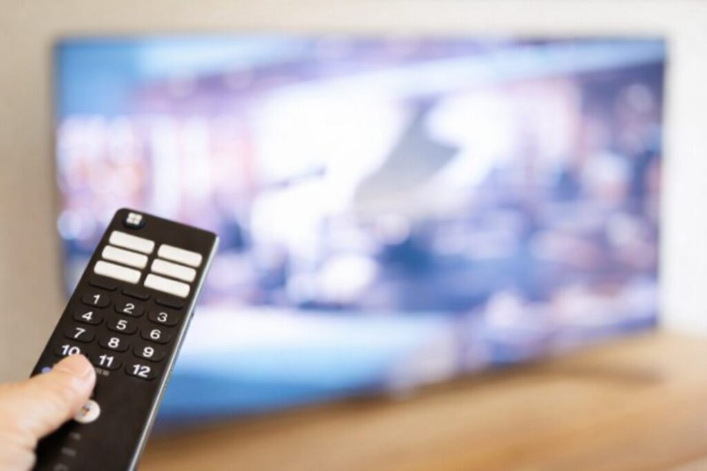 テレビに向けてリモコンを操作している手元の様子。画面はぼかされ、リモコンのボタン部分がはっきり写っている構図。