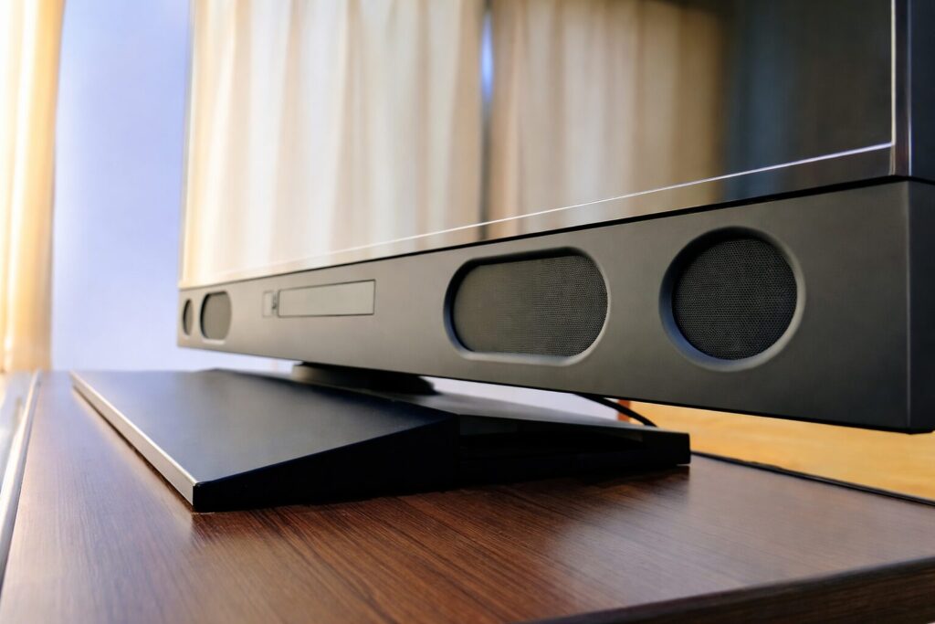 テレビ下部に内蔵されたスピーカー部分を横から捉えた様子。黒いテレビスタンドの上に設置され、前面には左右に丸型のスピーカーグリルが配置されている。