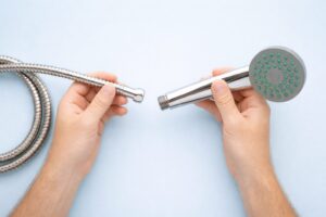 金属製のシャワーホースとハンドシャワーを両手で持ち、接続しようとしている様子を上から撮影したシンプルな構図の写真。