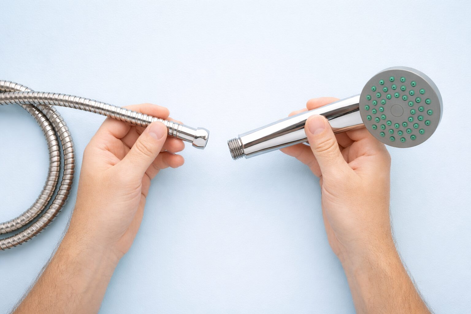 金属製のシャワーホースとハンドシャワーを両手で持ち、接続しようとしている様子を上から撮影したシンプルな構図の写真。