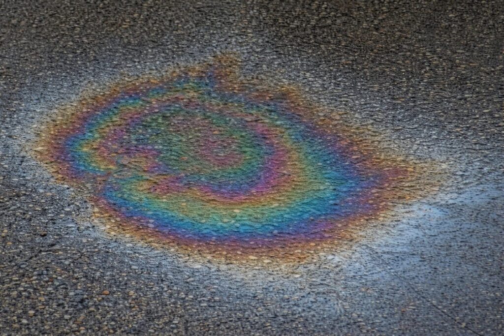 地面にこぼれた灯油がアスファルト表面に広がり、虹色の油膜模様が浮かび上がっている様子