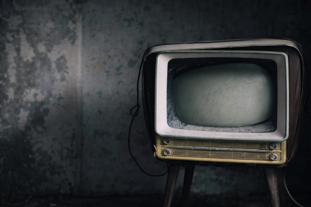 壁が劣化した暗い室内に置かれた、電源が入っていない古いブラウン管テレビを右寄りに配置し、左側に余白を持たせた静かな雰囲気の横長構図の写真