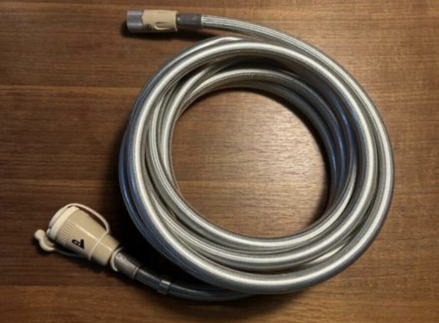 金属製のフレキシブルガスホースが木目のテーブル上に丸く巻かれ、両端に接続用のカプラと継手が付いている様子