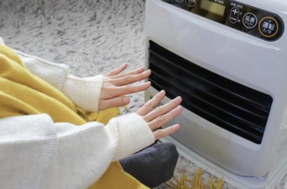 セーターをきた人が石油ファンヒーターで暖をとっている様子