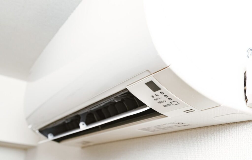 電気ストーブの前面に布団がかかり、接触部分から白い煙が立ち上っている様子。布団の一部は熱で変色しており、床に置かれた黒い電気ストーブの運転ランプが点灯している。