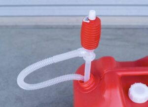 赤い灯油タンクの給油口に手動式の灯油ポンプを差し込み、透明な蛇腹ホースが接続されている状態を近距離から撮影した様子。