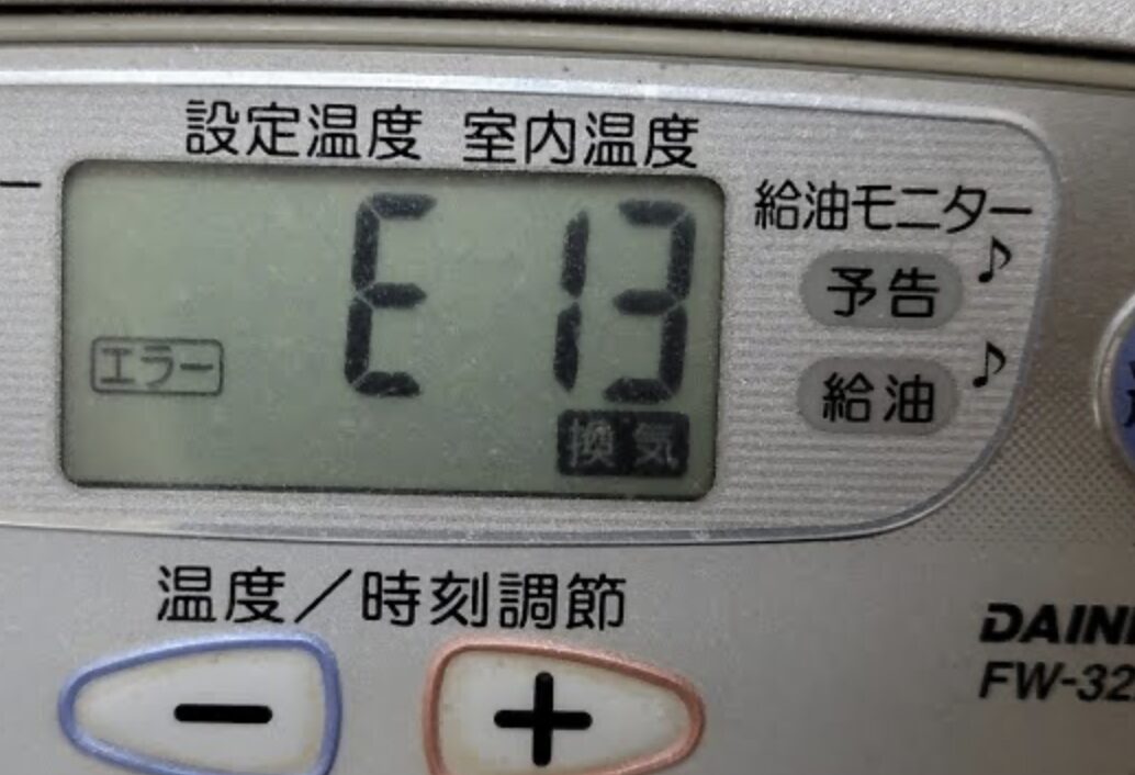 ダイニチ製の石油ファンヒーターの操作パネルに「E13」のエラー表示が出ており、設定温度・室内温度の表示欄や給油モニター、温度調節ボタンが確認できる状態を写した様子。