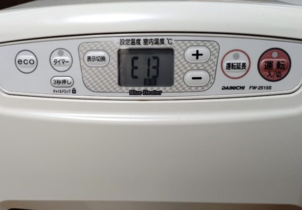 ダイニチ製の石油ファンヒーターの操作パネルに「E13」のエラー表示が出ており、運転入切ボタン、設定温度・室内温度の表示欄や給油モニター、温度調節ボタンが確認できる状態を写した様子。