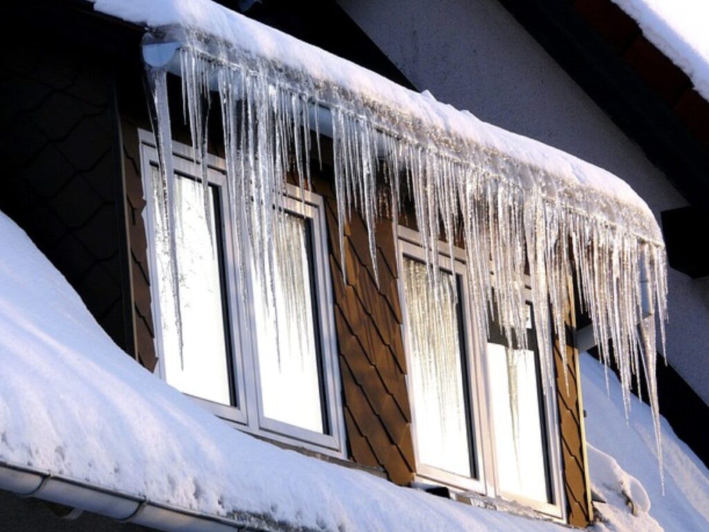 屋根の軒先に積もった雪から大きなつららが垂れ下がり、住宅外壁の窓まわりに凍結が発生している様子