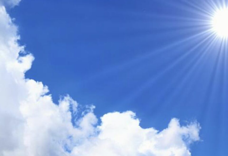 澄んだ青空に白い雲が広がり、右上から強い日差しが差し込んでいる様子を写した写真で、夏場の直射日光や強い輻射熱をイメージできる空の風景。