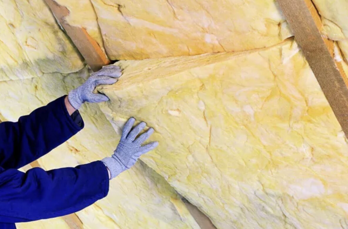 断熱施工中の建物内部で、木材の間にグラスウール系の断熱材を手袋をした作業員が押さえながら隙間なく充填している様子