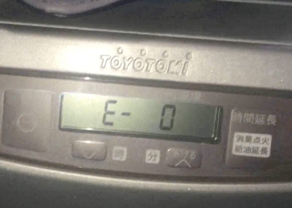 トヨトミ製石油ファンヒーターの操作パネルを正面から撮影した様子で、液晶画面にエラーコード「E-0」が表示され、本体上部にTOYOTOMIのロゴと時間設定・給油延長などの操作ボタンが確認できる状態