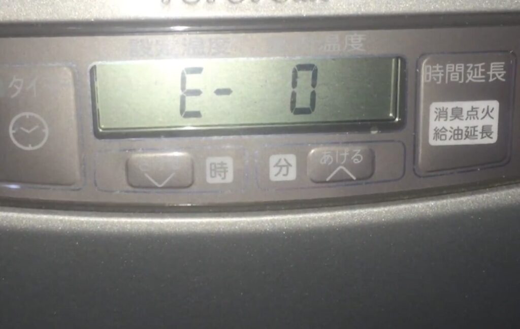 液晶表示部に「E-0」とエラーコードが表示された石油ファンヒーターの操作パネルを正面から撮影した様子で、周囲に時間設定や給油延長などの操作ボタンが配置されている状態