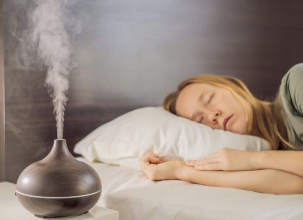 ベッドサイドに置かれた木目調の加湿器から白いミストが立ち上り、枕元で人物が穏やかな表情で眠っている寝室の様子