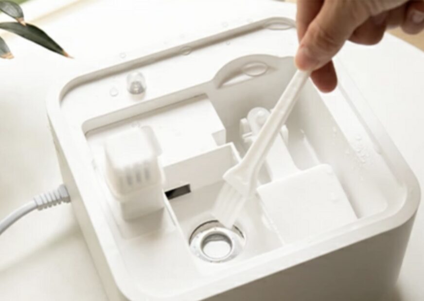上部カバーを外した加湿器の内部で、給水口まわりを細いブラシで清掃しているメンテナンス作業の様子