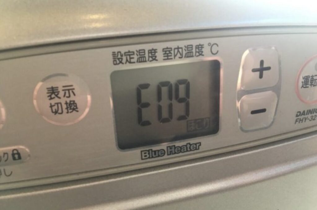 石油ファンヒーターの操作パネルを正面から撮影した様子で、液晶画面にエラーコード「E09」が表示されている状態。設定温度・室内温度の表示欄や、温度調整用のプラス・マイナスボタンが確認できる。
