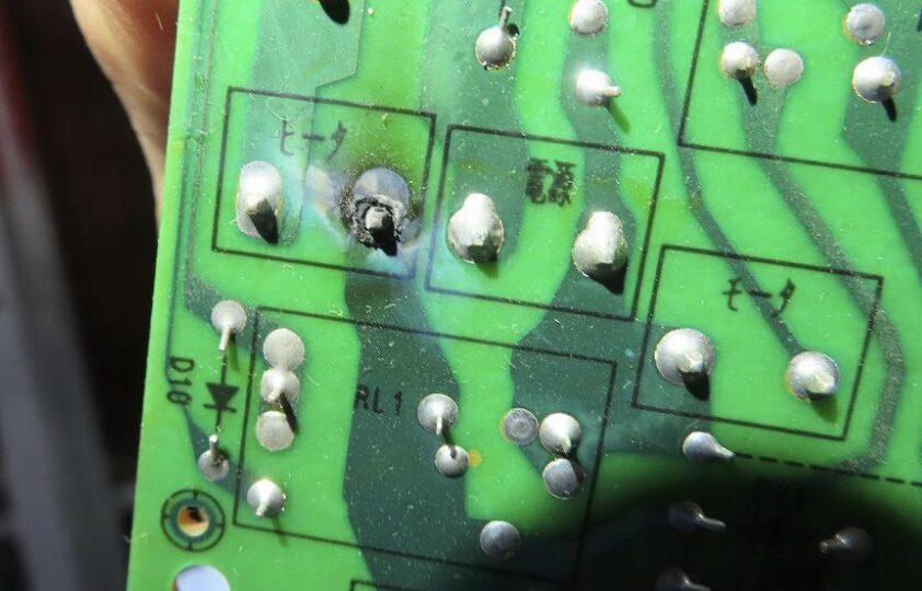 ダイニチ製石油ファンヒーター内部の制御基板を拡大撮影した様子。緑色のプリント基板上に多数のはんだ付けポイントがあり、一部のはんだ部分が黒く焦げたように変色している箇所が確認でき、熱や電気負荷の影響が疑われる状態が写っている。