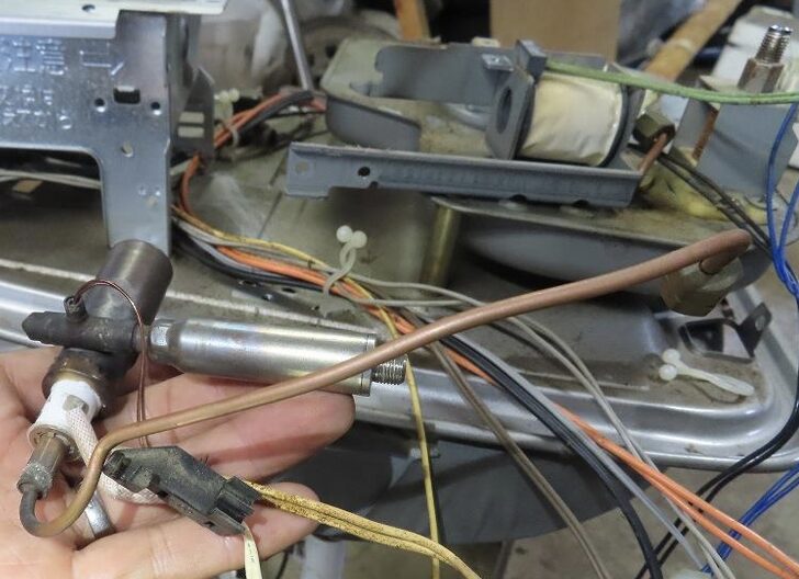 ダイニチ製石油ファンヒーターの内部を分解した状態で撮影した気化器の様子。灯油を霧化する金属製の気化器本体と銅製配管、接続された電線やセンサー類が確認でき、手で部品を持ちながら構造が分かる状態で写っている。