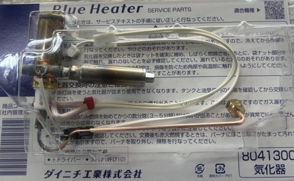ダイニチ工業の純正サービスパーツとして包装された石油ファンヒーター用の気化器部品。金属製の気化器本体に銅管や耐熱配線、コネクタが組み合わされ、交換用部品であることがわかる状態で透明パッケージ内に収められている。