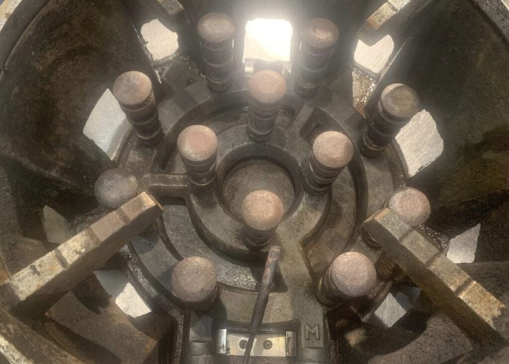 業務用ガスコンロのバーナー部分を上から撮影した様子。鋳物製の五徳と複数の炎口が円形に配置され、長年の使用による焦げ付きや油汚れが付着している状態が確認できる。