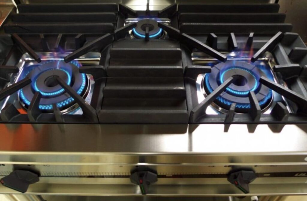 業務用ガスコンロの鋳物製バーナーを上から撮影した様子。複数の五徳に囲まれたバーナーから青い炎が均等に燃焼している状態が確認できる。