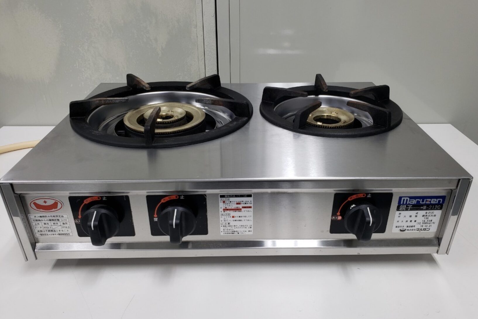 ステンレス製の卓上型業務用ガスコンロを正面から撮影した様子。2口の鋳物製バーナーと前面に配置された操作ノブが確認できるシンプルな構造。