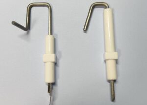 コロナ製石油ファンヒーターに使用されるフレームロッド部品を並べて撮影した様子。金属製のロッド先端がL字状に曲がっており、中央から下部にかけて白色の絶縁カバーが装着された構造が確認できる。燃焼時の炎検知に関わる部品の形状がわかる構図。