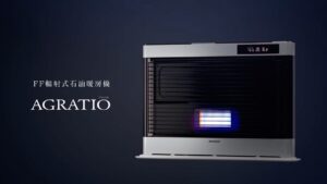 FF輻射式石油暖房機「AGRATIO」を正面から捉えた製品イメージ。ダークブルーの背景に、ブラックガラス越しの燃焼部と上部のデジタル表示が映える落ち着いたデザインが強調されている。