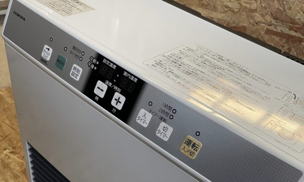 石油ストーブ上部の操作パネルと注意表示ラベルを上面寄りから撮影した様子。時刻設定、温度設定、タイマー関連の表記が確認できる。