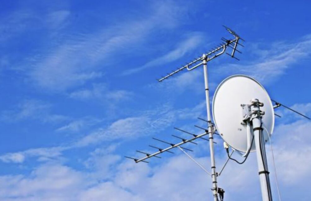 住宅屋外の屋根付近に設置された地デジアンテナと衛星放送用パラボラアンテナを青空背景で撮影した様子。