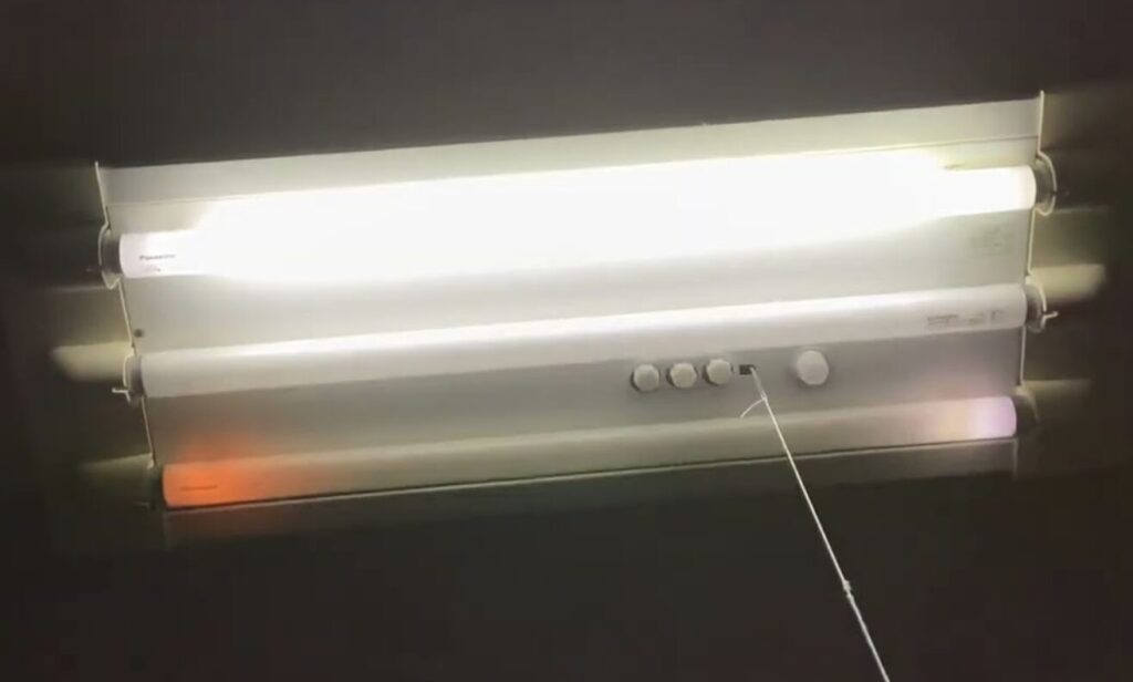 天井に設置された2灯式の直管蛍光灯器具が点灯している様子。ひもスイッチ付きで、住宅の室内照明として使用されている。