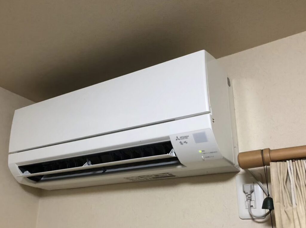 和室の壁上部に設置された白色の壁掛けエアコン本体を斜め下から撮影した様子。