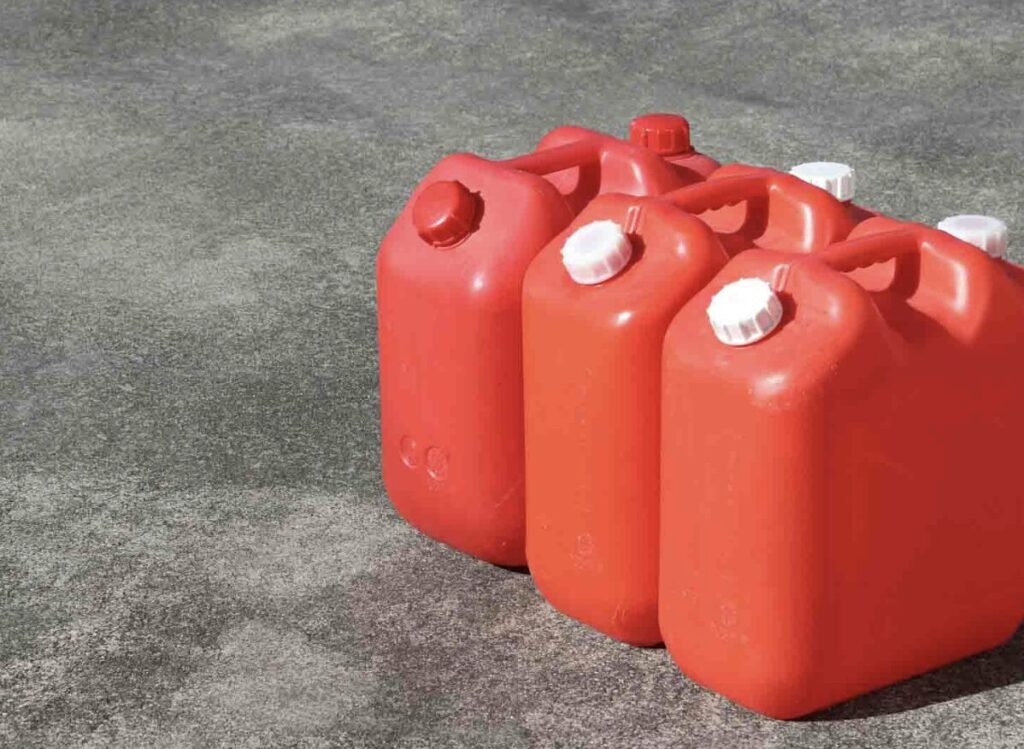 コンクリートの地面の上に赤色の灯油用ポリタンクが複数並べられている様子。白いキャップ付きのポリタンクが整列して置かれている。