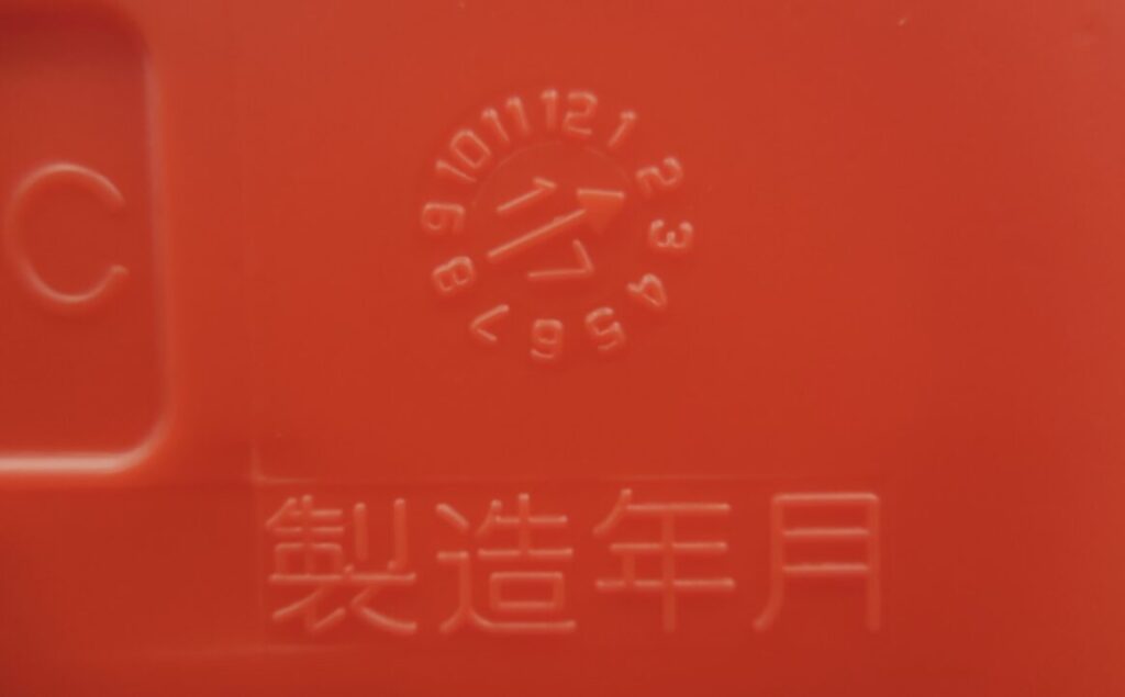 赤色の灯油用ポリタンク表面に刻印された製造年月表示の拡大写真。数字が円形に配置され、製造時期を示す矢印が確認できる。