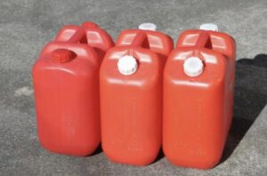 屋外の地面に赤色の灯油用ポリタンクが複数本並べて置かれている様子。白色や赤色のキャップが付いた一般家庭用ポリタンクが直立した状態で配置されている。