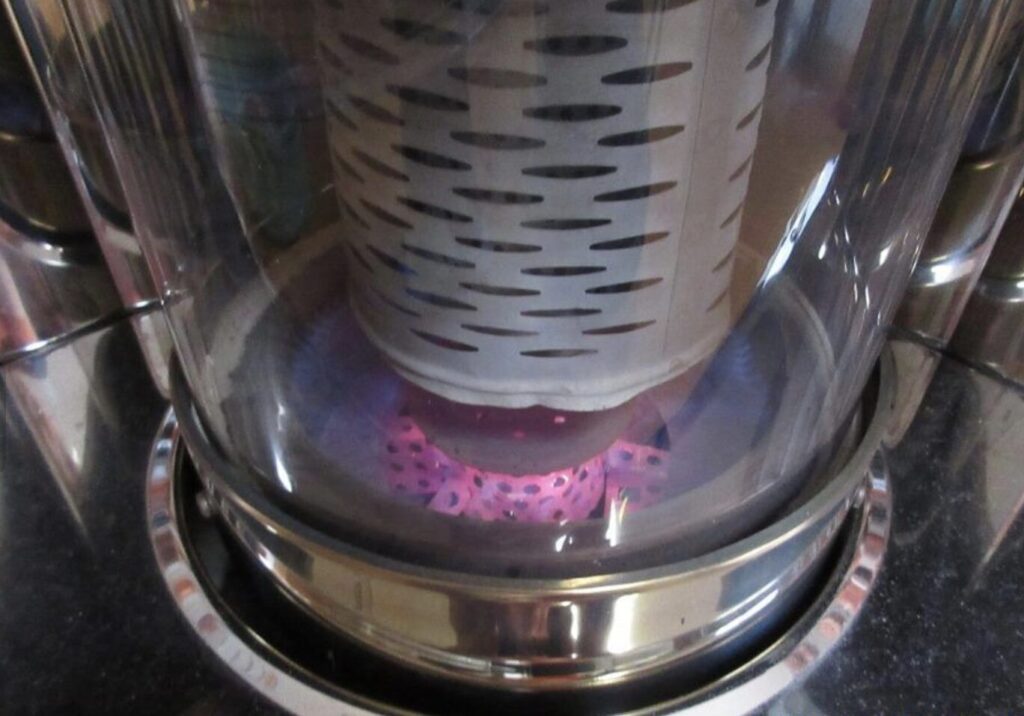 ガラス越しに見える石油ストーブの燃焼部。赤く加熱された点火ヒーターの周囲で青紫色の炎が安定して燃焼している状態。